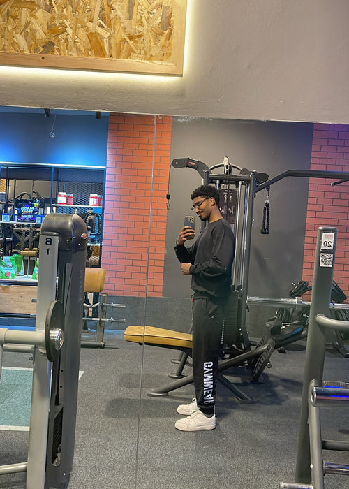 Person taking a selfie in a gym with exercise equipment and a colorful wall in the background.